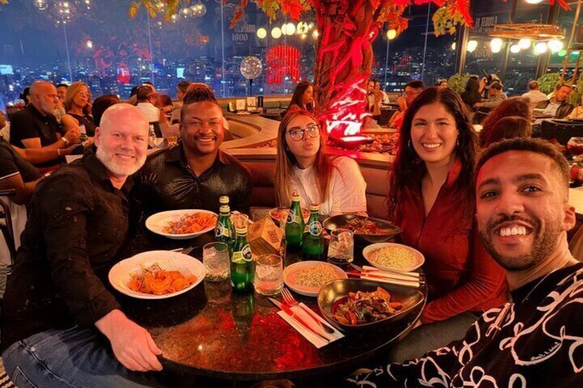 A group of people dining at a restaurant with a cityscape view. 1
