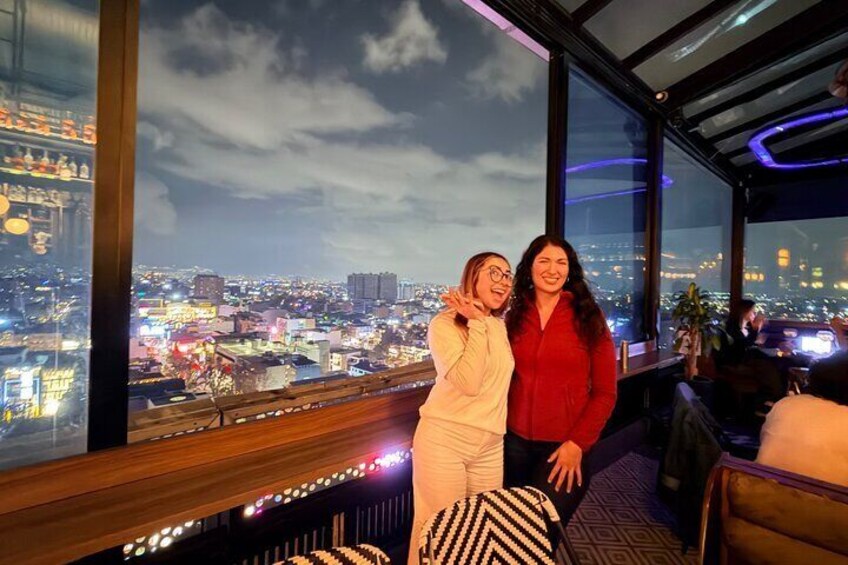 Two people standing by a window overlooking a cityscape at night. 4