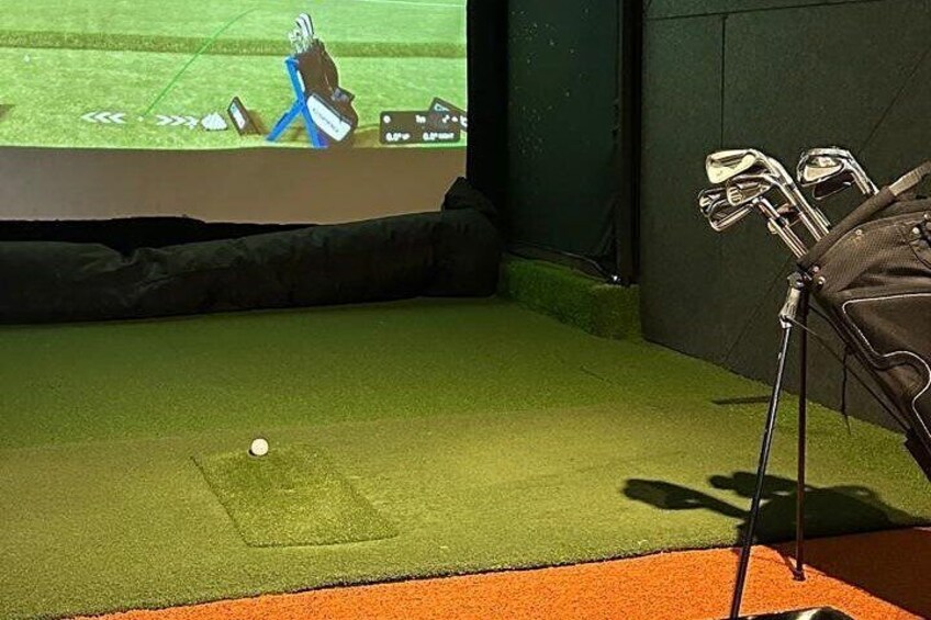 A golf practice area with a green mat, a golf ball, and a bag of clubs. 5