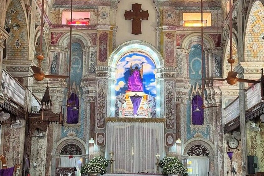 Ein prächtiger Kircheninnenraum mit einem zentralen Buntglasfenster, aufwändigen Wandverzierungen und einem Kruzifix über dem Altar. 2