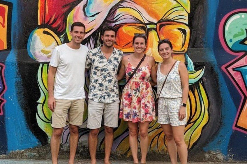 Eine Gruppe von Menschen steht vor einer bunten Graffiti-Mauer. 1