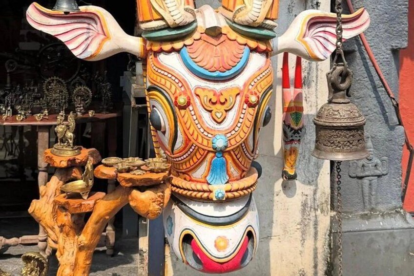 Eine farbenfrohe, aufwendig geschnitzte Holzmaske mit daran befestigter Glocke. 4