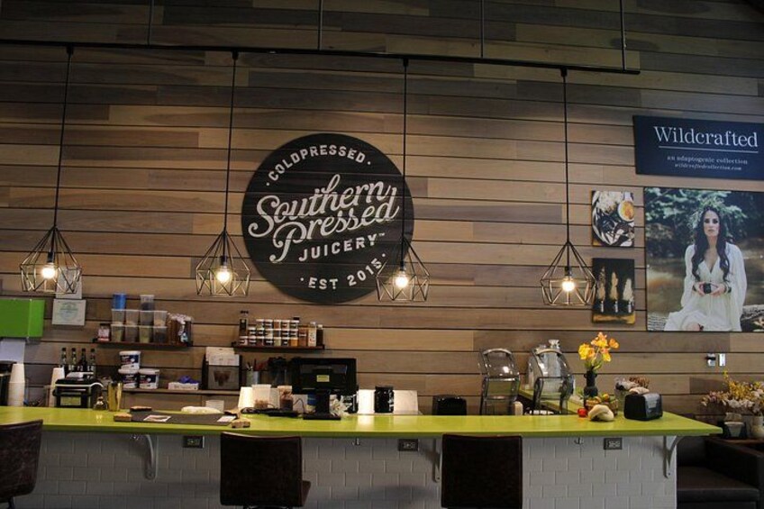 Interior de una cafetería con una pared de madera, un letrero que dice 'Southern Pressed Juicery' y un cartel de una mujer en un jardín. 2