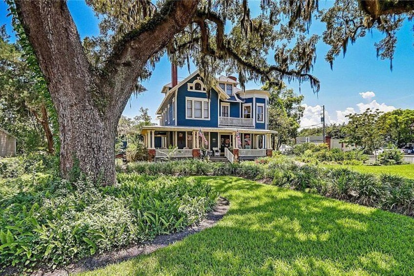 A two-story house with a porch, surrounded by lush greenery and a large tree. 5