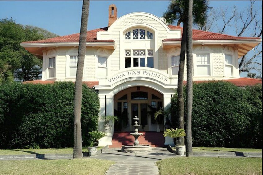 Villa Las Palmas with a red-tiled roof, arched entrance, and a fountain in the center. 2