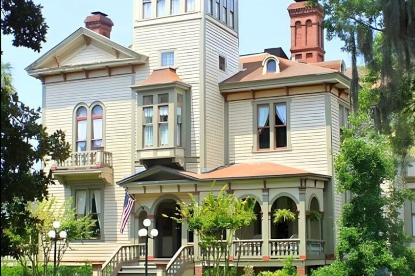 A large, historic house with multiple stories, a prominent tower, and a front porch with a railing. 3