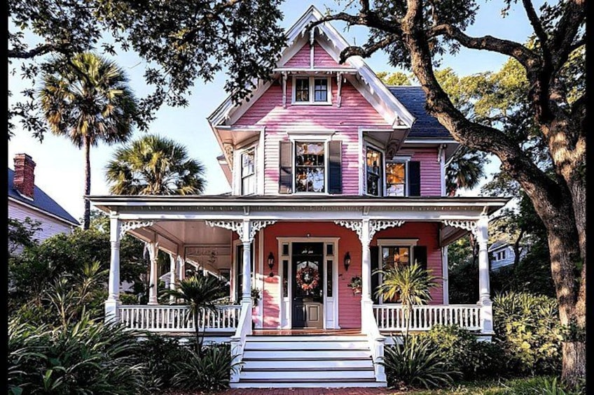 A pink house with a porch, surrounded by trees and plants. 2