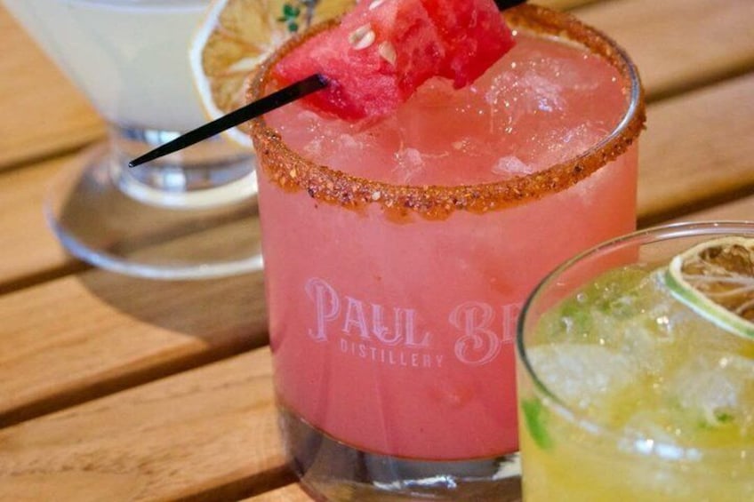 A pink cocktail with a strawberry garnish and a salted rim, labeled 'PAUL BE DISTILLERY,' on a wooden table. 4