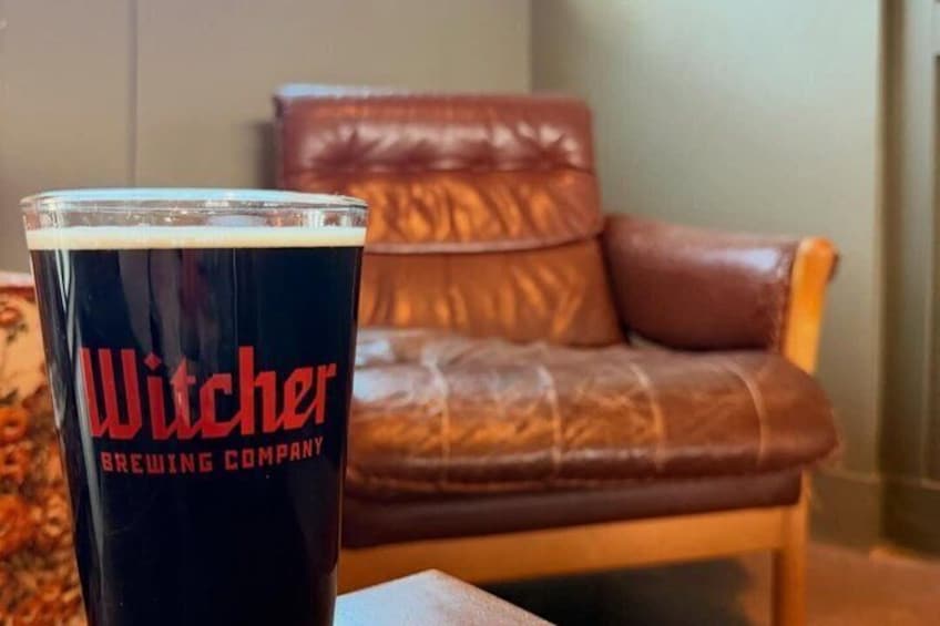 A glass of beer with 'Witcher Brewing Company' on it, a brown leather chair, and a wooden table. 3