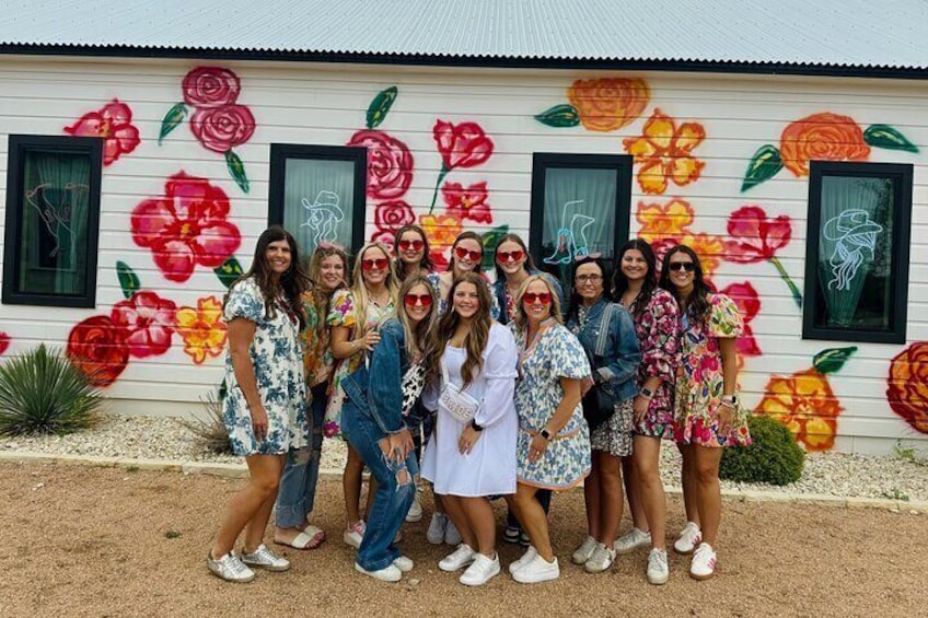 A group of people standing in front of a building with a floral mural. 1