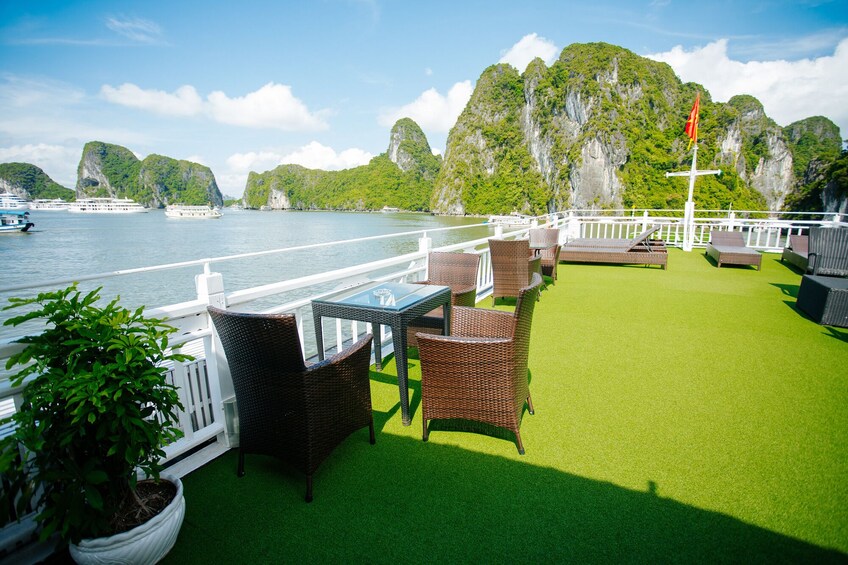 A deck with wicker furniture and a glass table overlooking a river with boats and limestone cliffs. 4