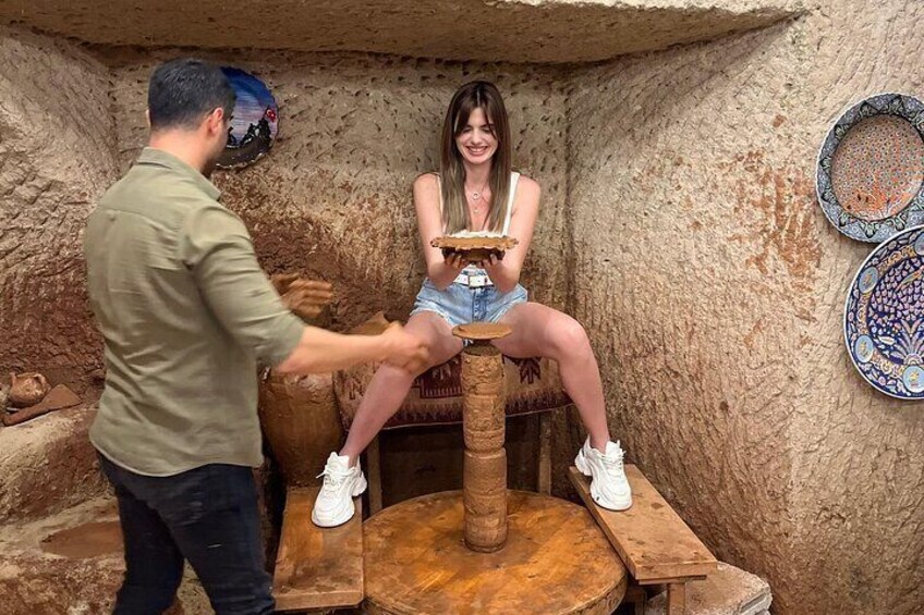 Una persona sentada en un taburete de madera en un espacio que recuerda a una cueva, con cerámica y platos decorativos en las paredes. 5