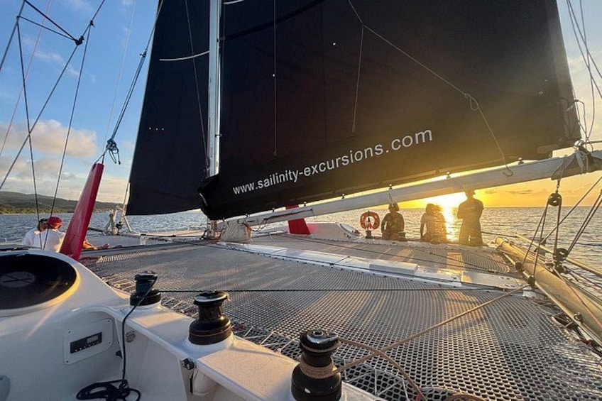 A sailboat with a website URL on the sail, a person standing on the deck, and a sunset in the background. 1