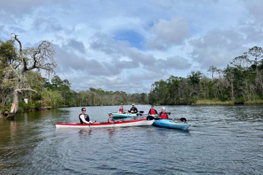 Three kayaks on a calm river surrounded by trees. 3