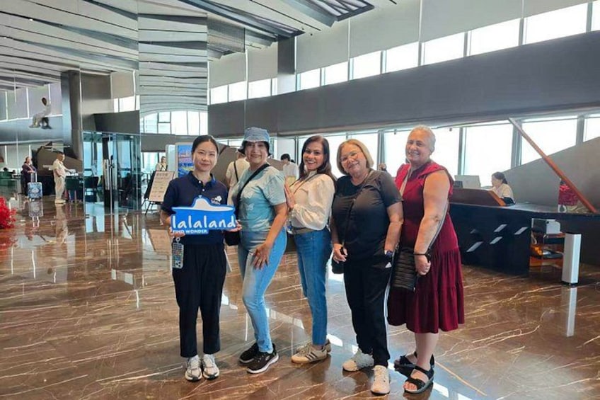 Un groupe de personnes se trouve dans un hall d’aéroport, et une pancarte indique « Lalaland ». 3