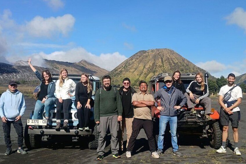 A group of people standing in front of a vehicle with a mountainous background. 1