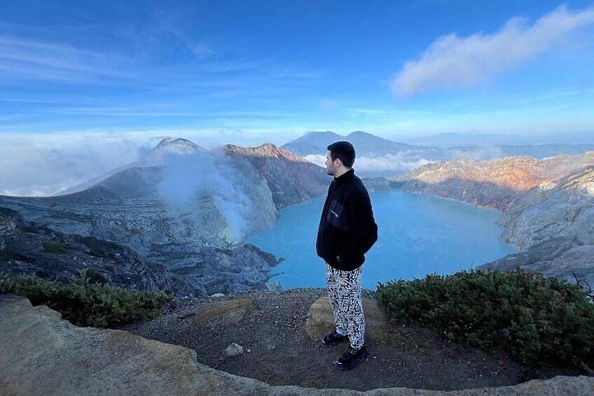 A person standing on a rocky outcrop overlooking a lake with mountains in the background. 4