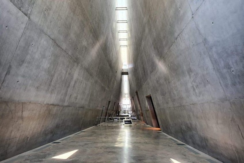 A long, narrow concrete corridor with a high ceiling and skylights. 5
