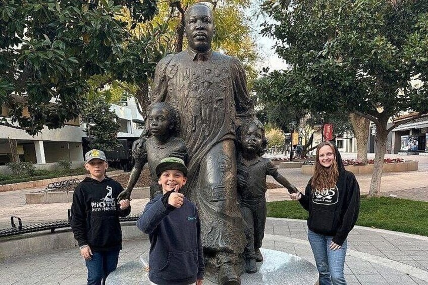 A statue of a man with children, surrounded by trees and a paved area. 3