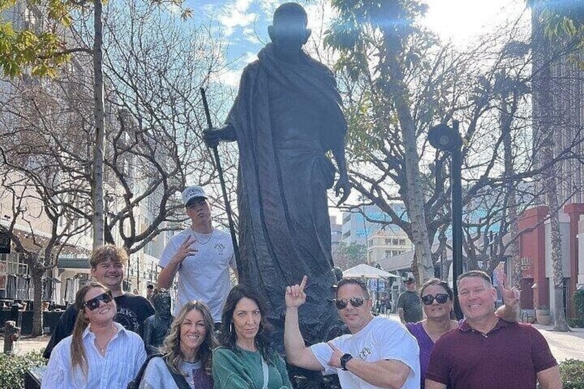 A group of people posing in front of a statue in an urban setting with trees and buildings in the background. 2