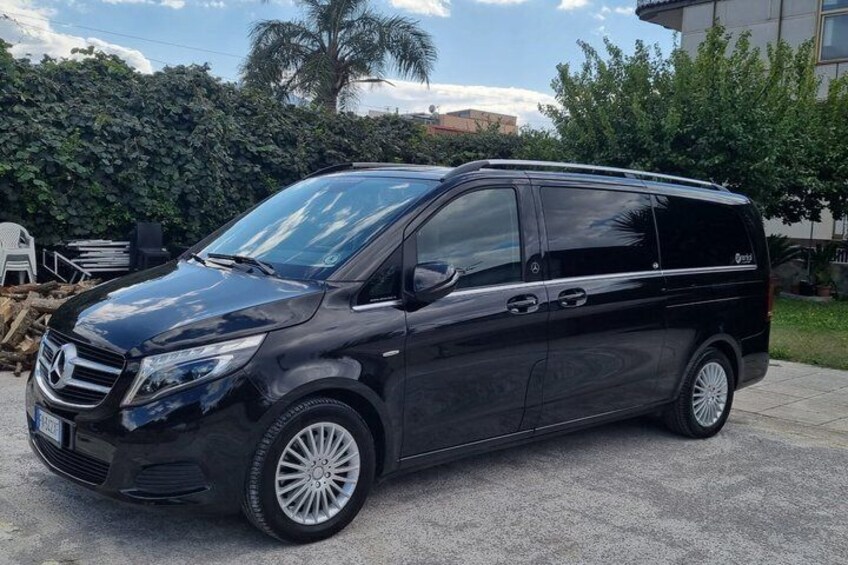 Ein schwarzer Mercedes-Benz Sprinter steht auf einer Betonfläche, im Hintergrund sind ein Hecken und Palmen zu sehen. 2