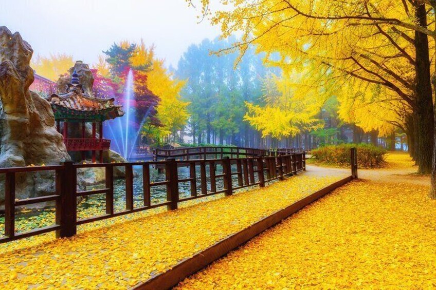 Ein Park mit einem traditionellen Pavillon, einer steinernen Löwenstatue, einem Springbrunnen und einem mit gelben Blättern bedeckten Weg. 5