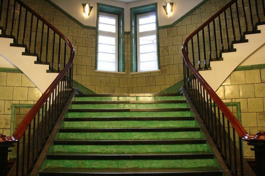 Un escalier avec des marches vertes, des rampes en bois et deux fenêtres à cadre vert. 3