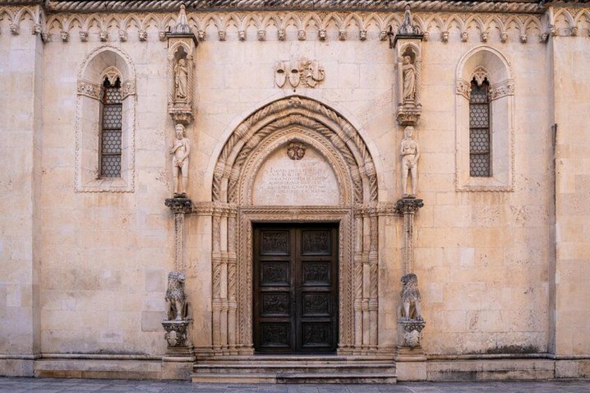 A building with a large arched entrance, statues on either side, and a decorative frieze above the door. 4