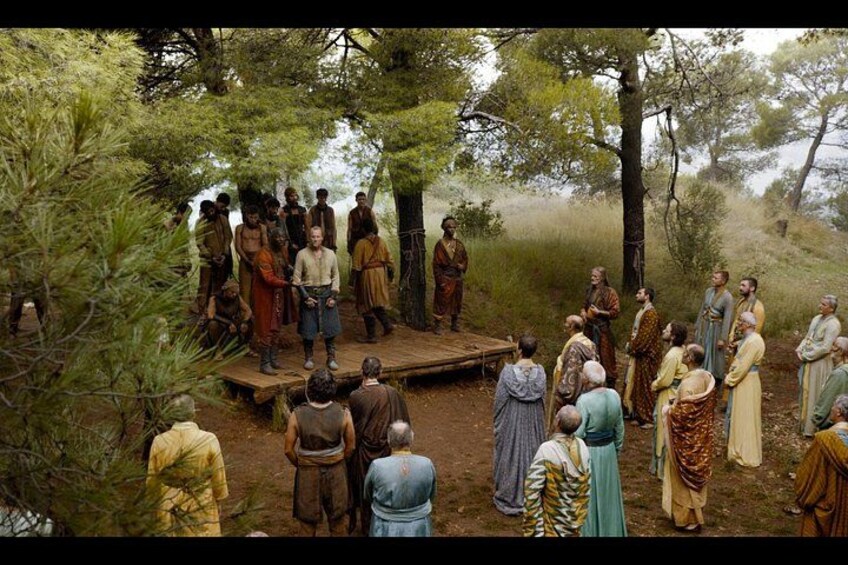 A group of people gathered around a wooden platform in a forested area. 2