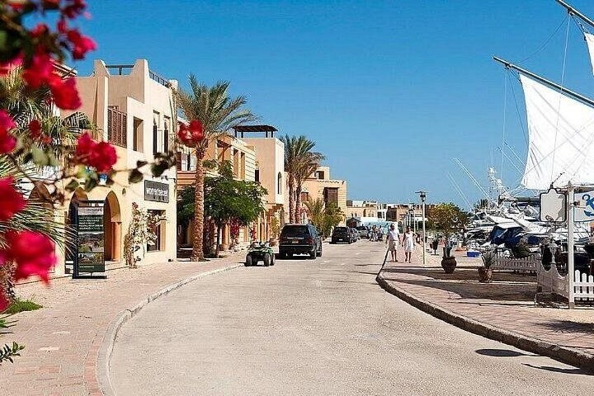 A coastal street with buildings, parked cars, and sailboats. 2