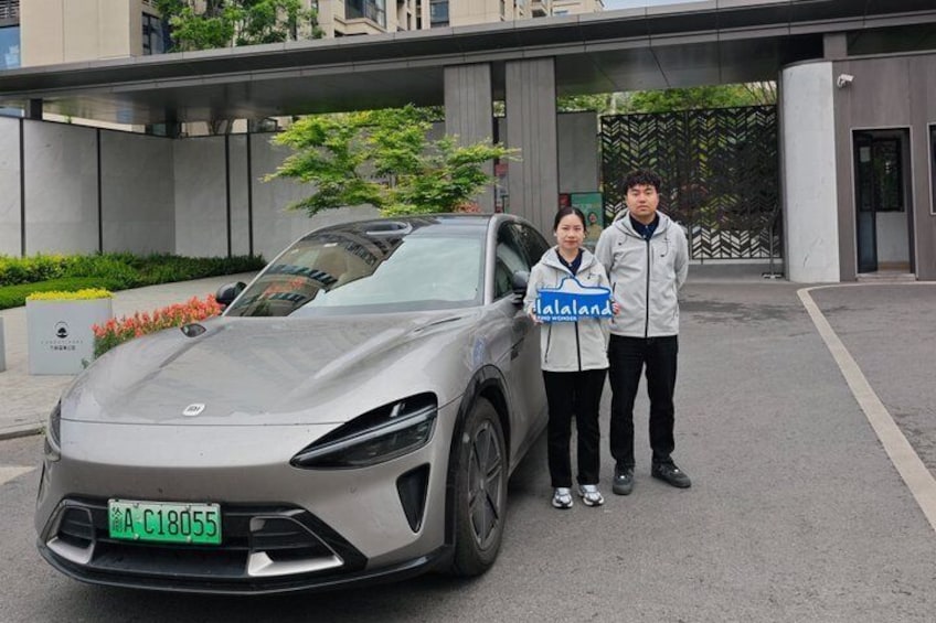 Une voiture de sport argentée est garée devant un bâtiment moderne, et deux personnes se tiennent à côté. 5