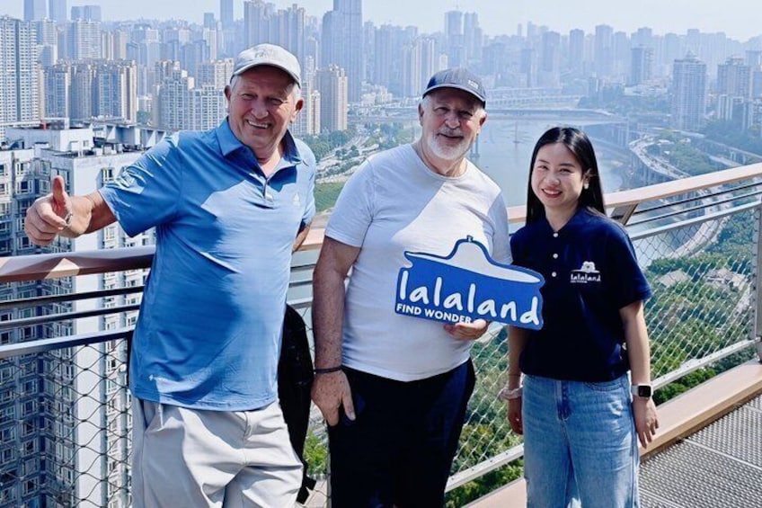 Trois personnes se tiennent sur un pont, avec la silhouette d’une ville en arrière-plan. 2