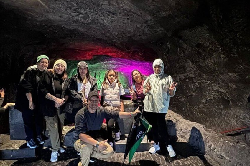 A group of people posing in a cave with colorful lighting. 1