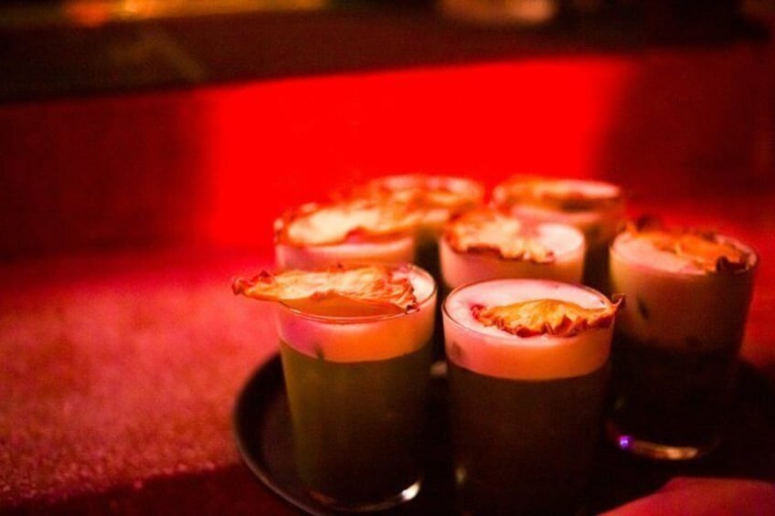 Ein Tablett mit Getränken mit schaumiger Oberfläche, vermutlich Cocktails, in gedämpftem Licht. 2