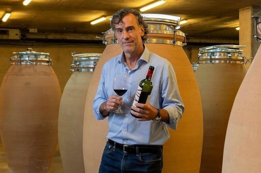 Eine Person hält eine Weinflasche und ein Glas in einem Keller mit großen Weinfässern. 5