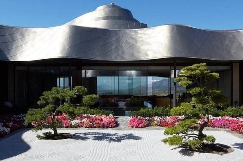 Ein modernes Gebäude mit einem gewölbten Metall-Dach, umgeben von einem Garten mit Bonsai-Bäumen und rosa Blumen. 4