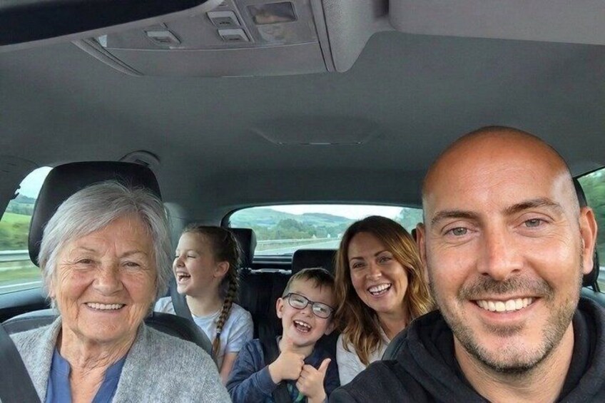 En familie i bil med et bjergrigt landskab i baggrunden. 2