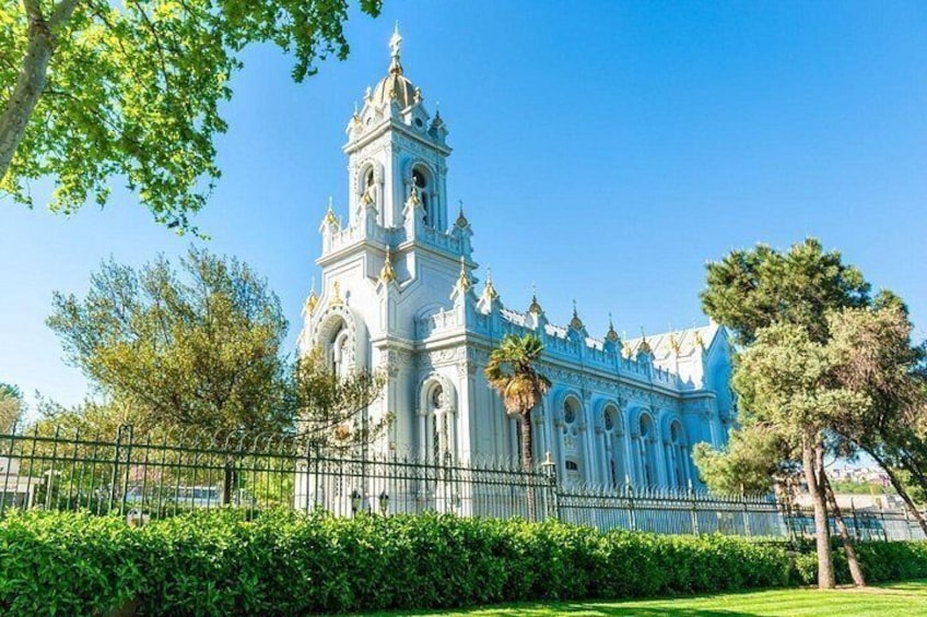 Een witte kerk met een klokkentoren, omgeven door groen en een hek. 3