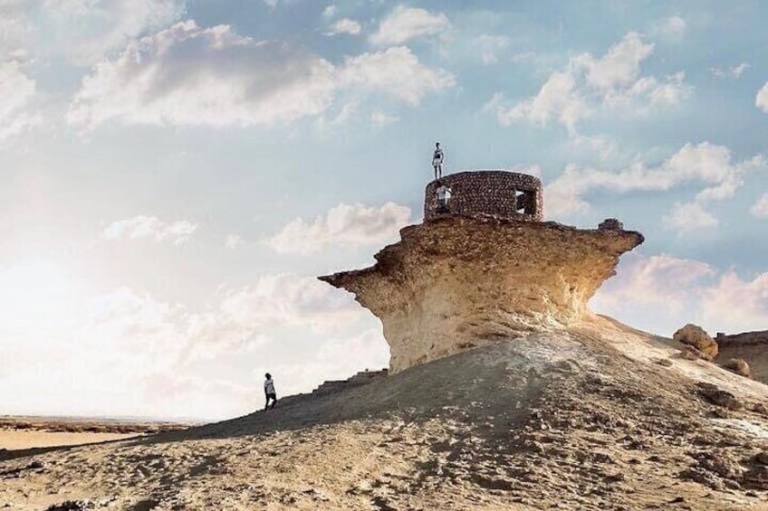 A person standing on a large rock formation with a structure on top. 3