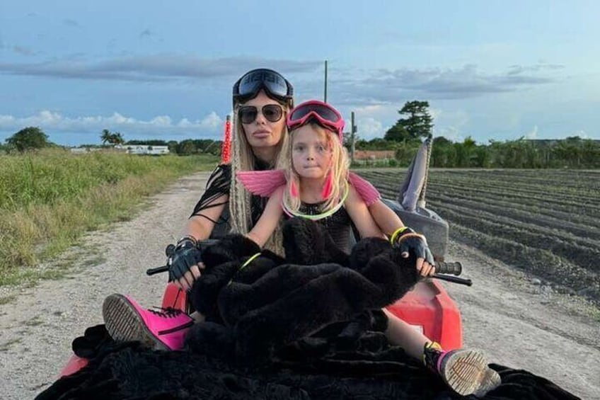 Two people on a red ATV on a dirt road with fields in the background. 4