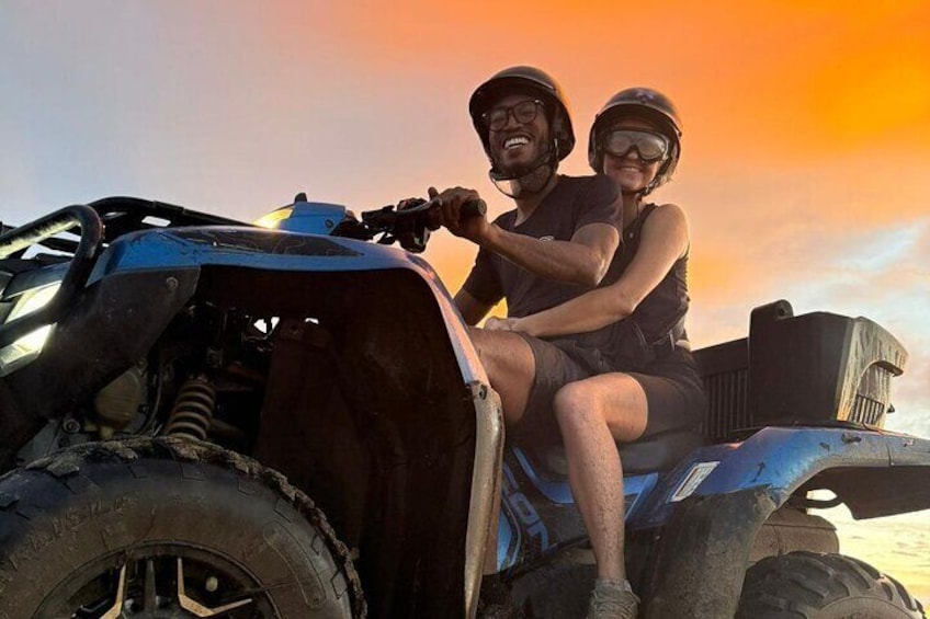 Two people on a blue ATV with a sunset in the background. 3