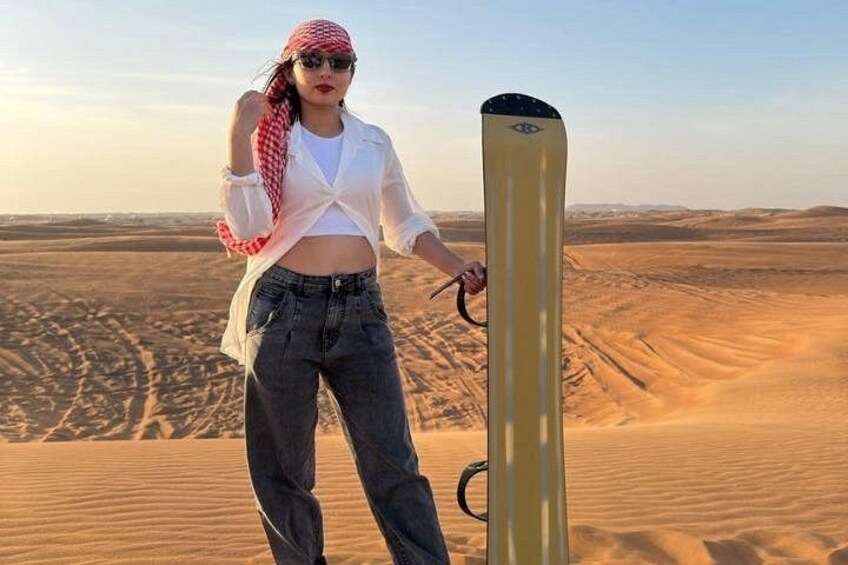 Eine Person steht mit einem Snowboard auf einer Sanddüne. 3