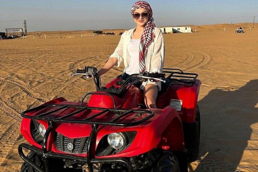 A person riding a red ATV in a desert with sand dunes and a clear sky. 3