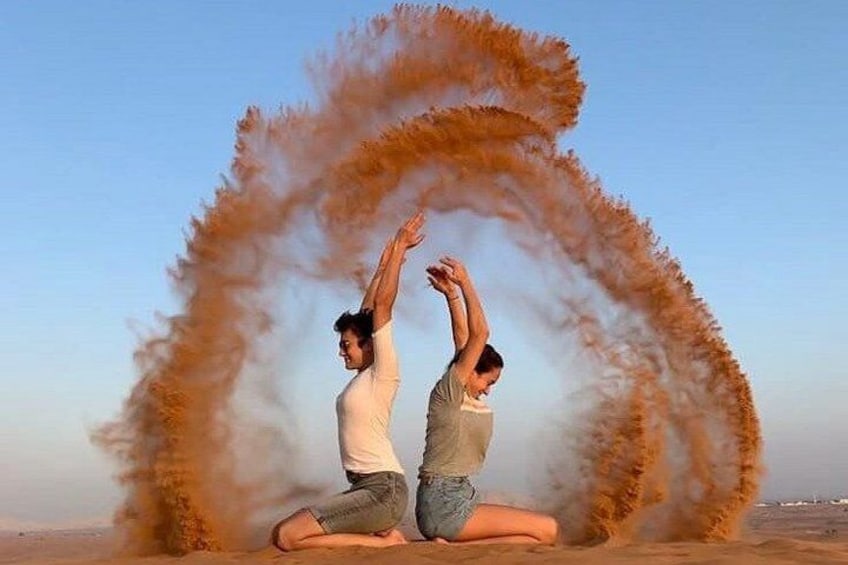 Two people performing a yoga pose on a beach with a large dust cloud around them. 2