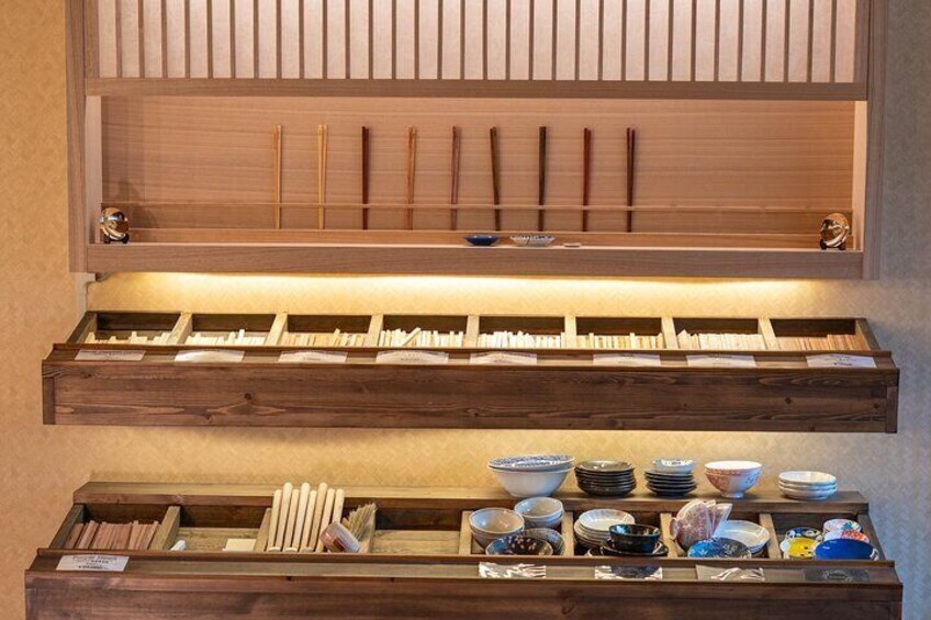 A wooden shelf with chopsticks, bowls, and plates. 5