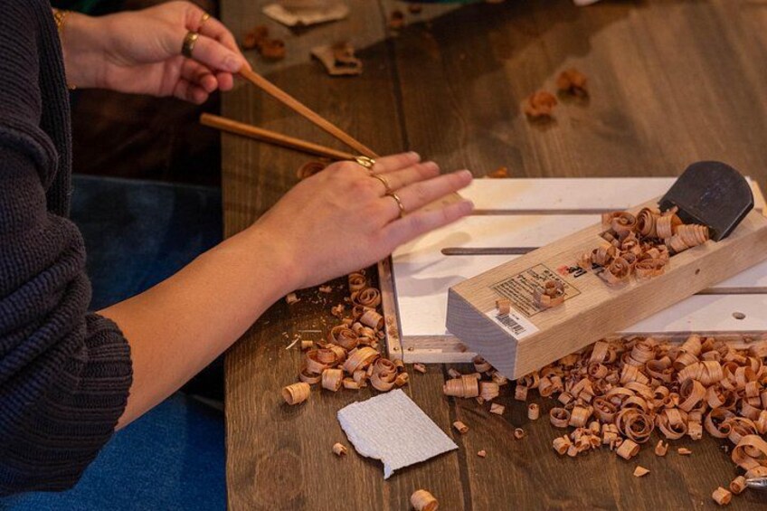 Des mains utilisent des baguettes pour manipuler des copeaux de bois sur une table. 5