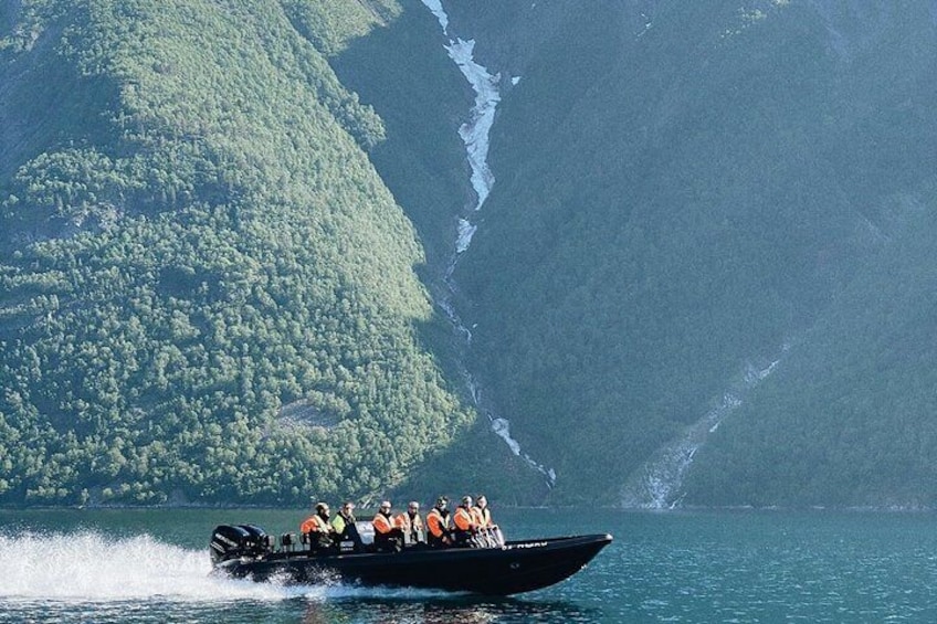 A speedboat with passengers on a lake with mountains in the background. 1