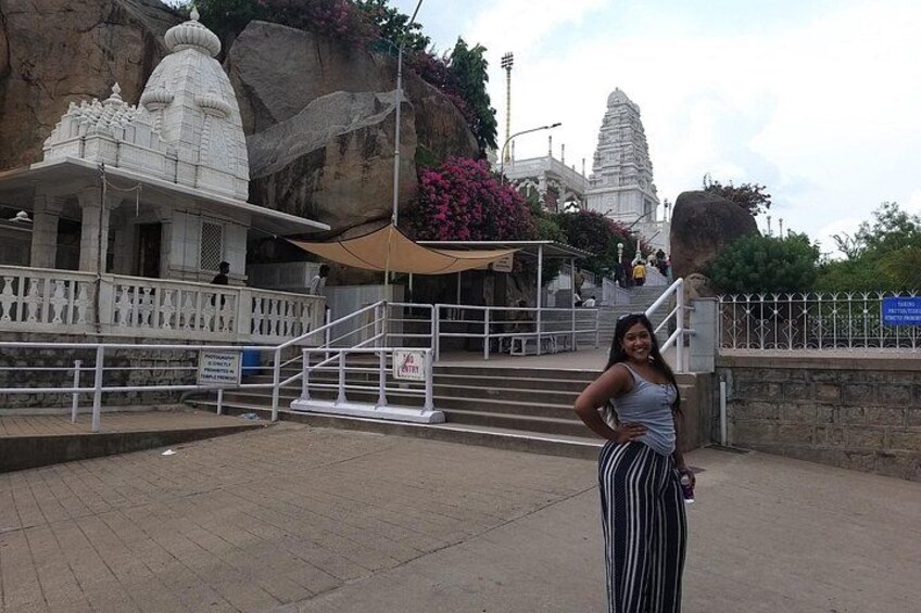 A temple complex with steps leading up to a shrine, a large rock formation, and a clear sky. 3