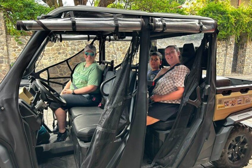En golfbil med två passagerare, en stenmur och grönska i bakgrunden. 2