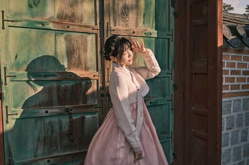 A person in a pink dress standing in front of a green wooden door. 1